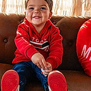 Oliver is registered to the contest to win money with this photo: child, toddler, smiling, red_hoodie, sneakers, couch, indoor, portrait, happy, cute, macrame_curtain, window, casual_clothing, seated, playful, young_child, face, hands, feet, home