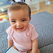 Mélina participe au concours pour gagner de l'argent avec cette photo : baby, blanket, bright, child, cute, hair_ties, happy, home, indoor, infant, person, pink_clothing, playful, portrait, purple, seated, smiling, soft_texture, toy_book, young