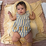 Estefany is registered to the contest to win money with this photo: baby, child, infant, face, headband, clothing, socks, pillow, blanket, bed, soft_texture, striped, yellow, blue, cute, indoors, portrait, laying_down, expression, skin