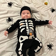 Sasha participe au concours pour gagner de l'argent avec cette photo : baby, child, costume, skeleton, black_clothing, white_blanket, toy_spiders, pumpkin, halloween, cute, lying_down, infant, smiling, headwear, indoors, playful, holiday, decorations, person, festive
