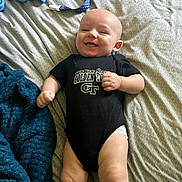 Allen is registered to the contest to win money with this photo: baby, bed, blanket, clothing, comfort, cute, fabric, foot, hand, happy, head, indoors, infant, lying_down, onesie, pacifier, person, skin, smiling, toddler