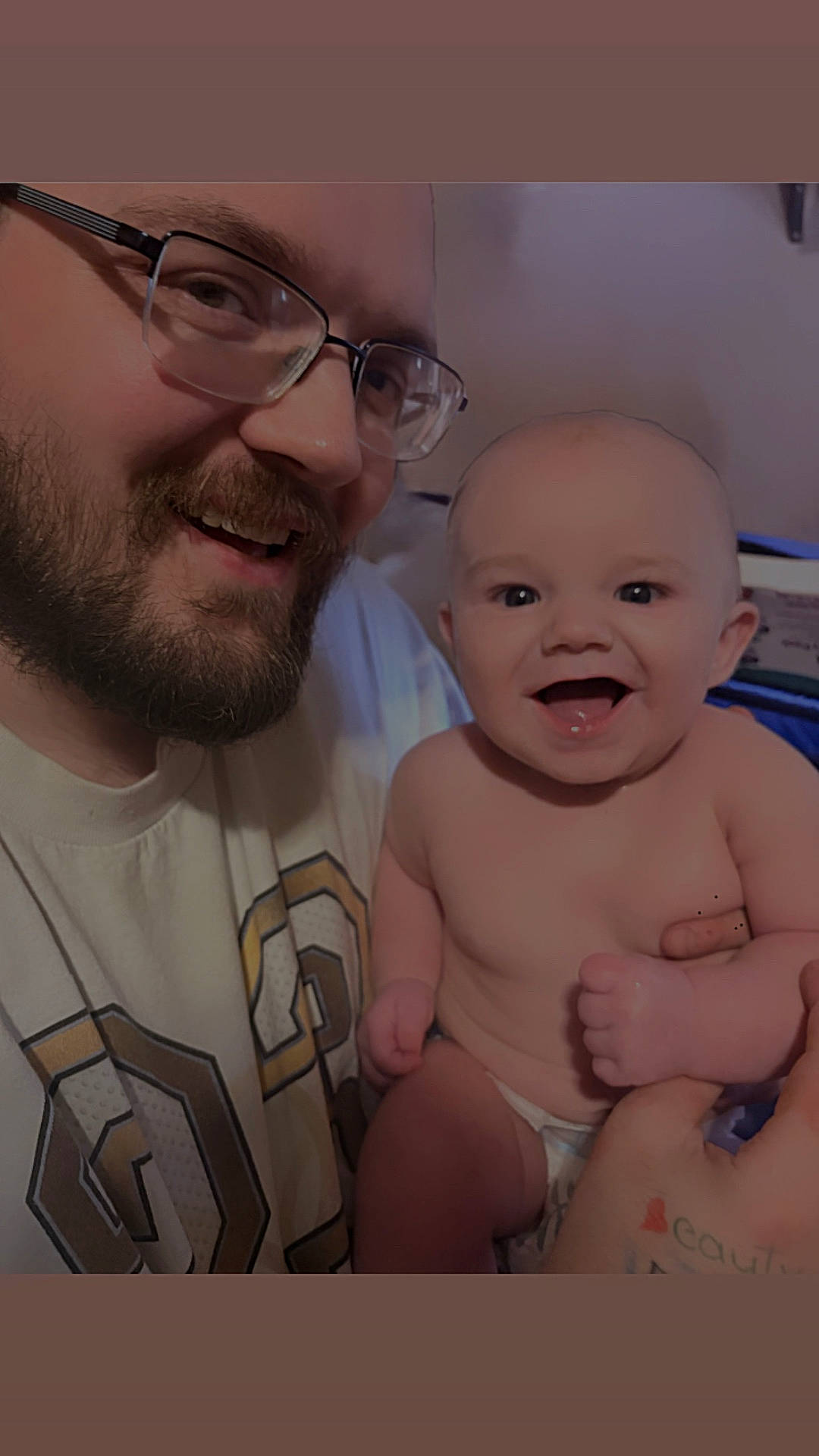 baby, beard, casual, child, closeup, diaper, expression, face, glasses, hand, happy, holding, indoor, joy, man, parent, person, skin, smile, tattoo