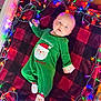 baby, child, infant, green_onesie, christmas_lights, red_black_blanket, floor, festive, holiday, cute, lying_down, indoors, face, feet, wooden_floor, colorful_lights, holiday_outfit, santa_claus, cozy, portrait
