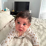 Luca joined the competition — help win amazing prizes! baby, infant, crawling, onesie, teddy_bear_pattern, blanket, bed, bedroom, television, curly_hair, cute, child, person, indoor, soft_light, white, expression, face, eyes, cozy