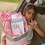 child, girl, bunny_ears, peace_sign, easter_basket, hello_kitty, paint_set, lip_moisturizer, car, car_door, seat, outdoor, grass, tree, fence, toy, pink, silver, cute, holiday