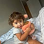 Evelyn joined the competition — help win amazing prizes! toddler, child, plush_toy, bed, curly_hair, indoor, white_bedding, soft_toy, cute, smiling, person, cozy, room, curiosity, sitting, casual_clothing, young_child, home, playful, portrait