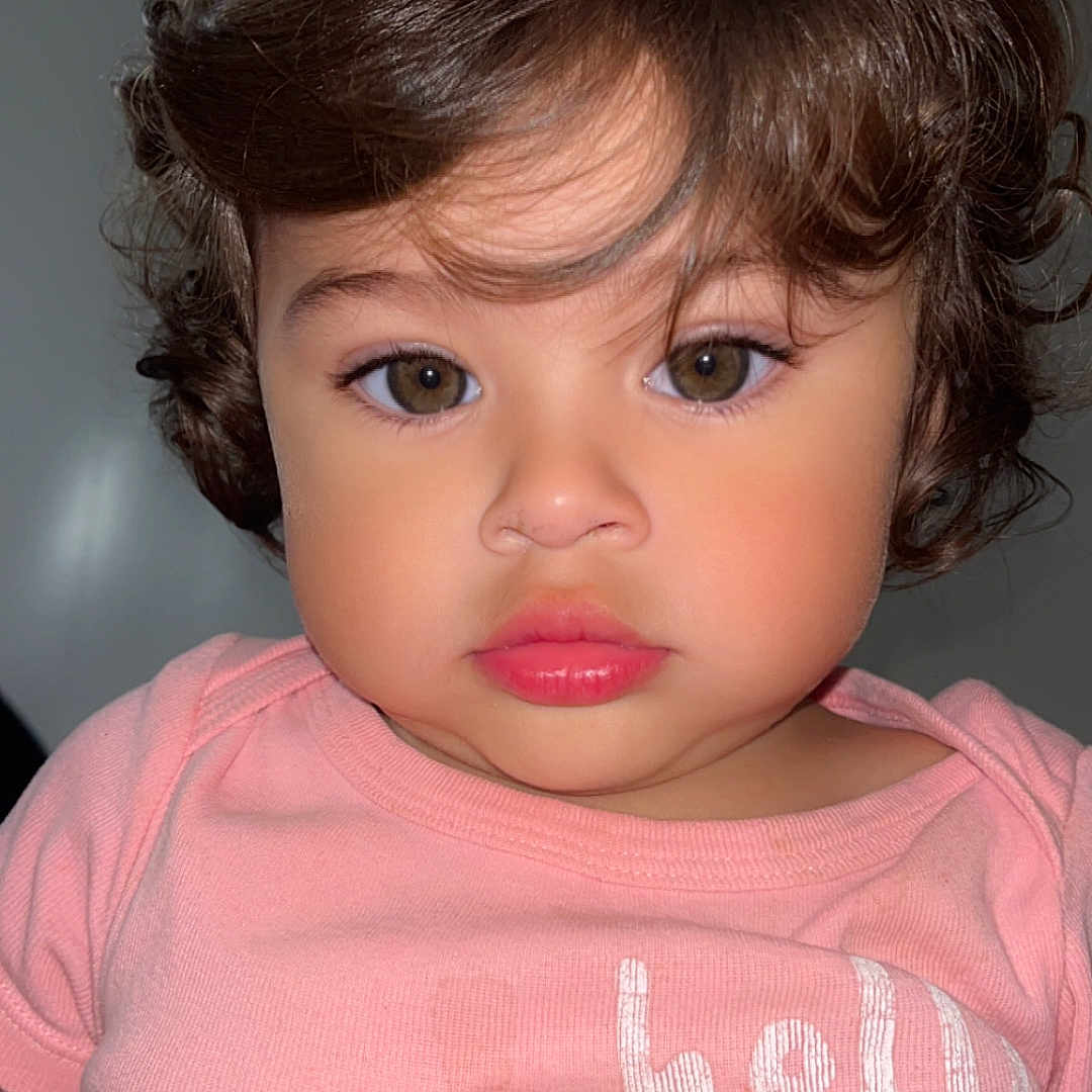 Evelyn is registered to the contest to win money with this photo: baby, casual, child, closeup, clothing, curly_hair, cute, expression, eyelashes, face, head, human, indoor, looking_at_camera, person, pink_shirt, portrait, skin, toddler, young_child