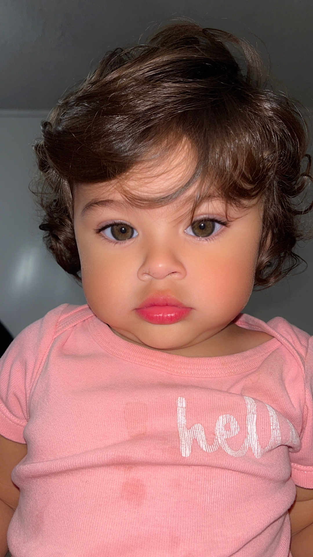 Evelyn is registered to the contest to win money with this photo: toddler, child, portrait, face, curly_hair, pink_shirt, expression, indoor, person, young_child, closeup, baby, cute, eyelashes, skin, clothing, head, looking_at_camera, human, casual