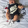 apparel, baby, baby_boy, blanket, child, clothing, cute, fashion, footwear, hat, indoors, infant, lying_down, nike, numbers, person, portrait, smiling, sneakers, socks