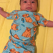Amari is registered to the contest to win money with this photo: baby, infant, child, blue_clothing, cartoon_print, yellow_background, pacifier, lying_down, cute, face, arms_outstretched, sleepwear, patterned_clothes, indoors, soft_lighting, playful, expression, comfort, bed, rest