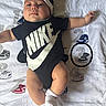 Amari is registered to the contest to win money with this photo: apparel, baby, black, blanket, child, clothing, cute, footwear, hat, indoor, infant, lying_down, nike, numbers, onesie, portrait, sneakers, socks, soft_texture, white
