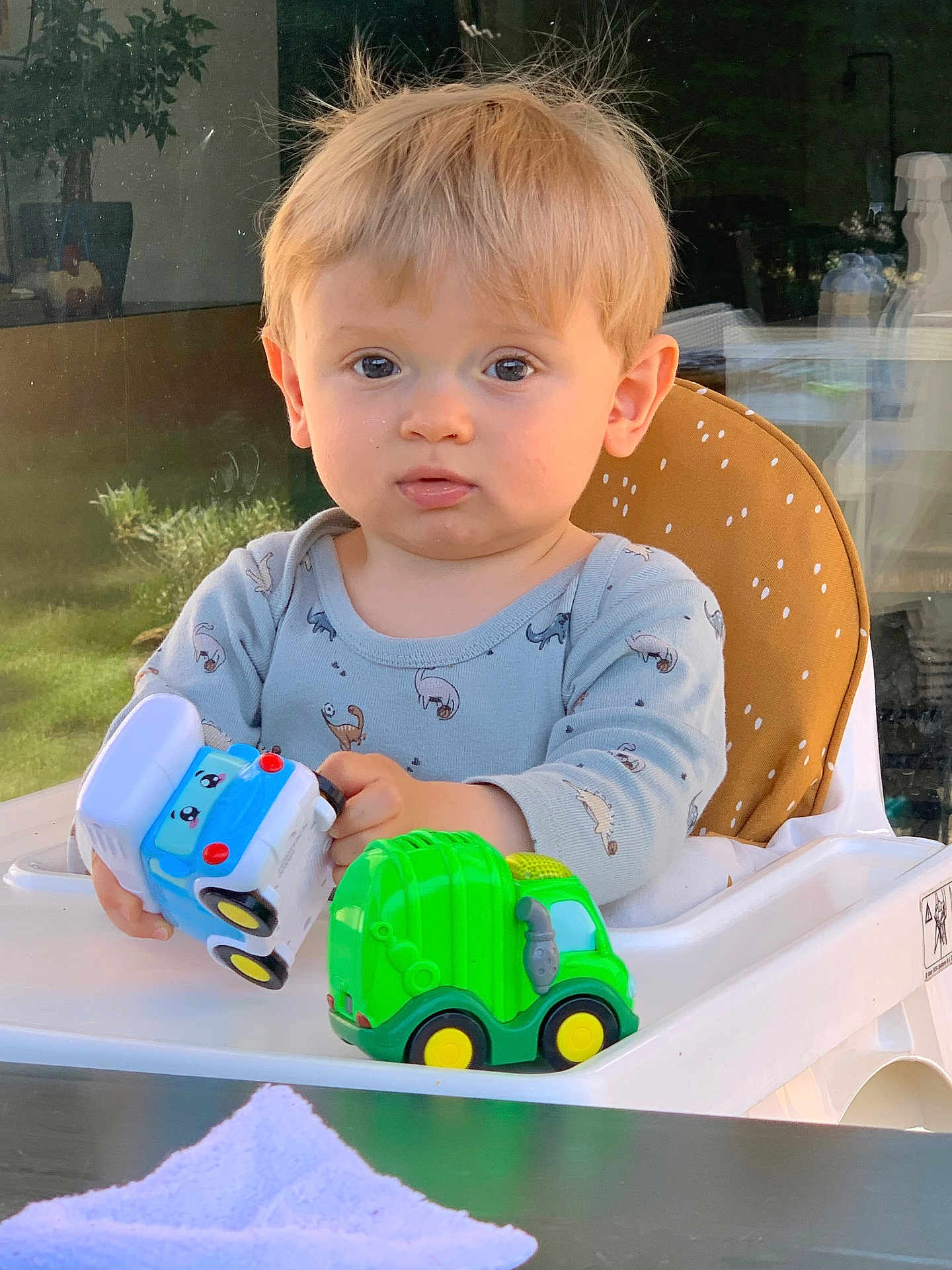Sandro a rejoint le concours — aidez-le/la à gagner de superbes lots ! toddler, child, toy, high_chair, blond_hair, indoor, window, curious, blue_clothing, plastic_toys, green_toy, white_high_chair, face, person, baby, cute, young_child, playing, expression, seated