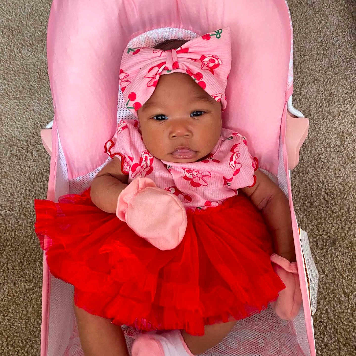 Meilani joined the competition — help win amazing prizes! baby, infant, child, pink_bow, red_tutu, mittens, baby_seat, pink_seat, carpet, cute, portrait, indoors, clothing, fashion, adorable, smiling, person, headwear, feet, sitting