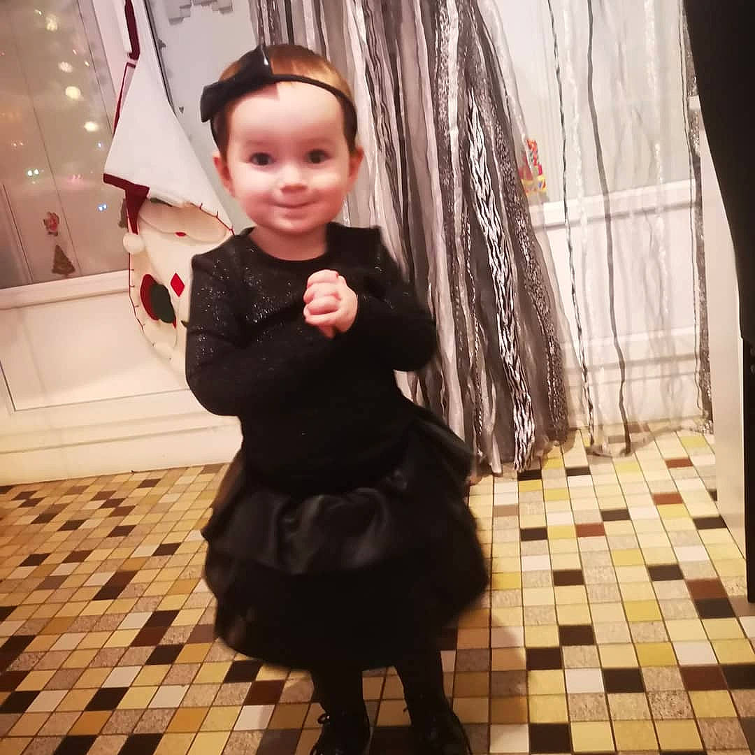 Jade a rejoint le concours — aidez-le/la à gagner de superbes lots ! baby, black, costume, curtain, day_dress, floor, flooring, hair_accessory, joy, little_black_dress, one_piece_garment, person, square, tile, toddler, window_treatment