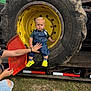 Cameron is registered to the contest to win money with this photo: child, toddler, yellow_shoes, denim_overalls, tractor_tire, large_tire, outdoor, grass, hand, person, vehicle, wheel, yellow, blue_clothing, casual, dirt, support, young_child, jeans, footwear