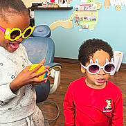 Mercedes joined the competition — help win amazing prizes! child, children, sunglasses, yellow_sunglasses, bunny_sunglasses, playful, red_sweater, gray_sweatshirt, toy_ball, indoor, wood_floor, dental_chair, wall_art, smile, happy, person, kids_room, curly_hair, glasses, fun