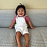 Sebastian is registered to the contest to win money with this photo: toddler, child, smiling, happy, sitting, couch, checkered_pattern, overalls, striped_shirt, barefoot, indoor, person, hair, face, joy, cute, young_child, plaid, furniture, casual_clothing