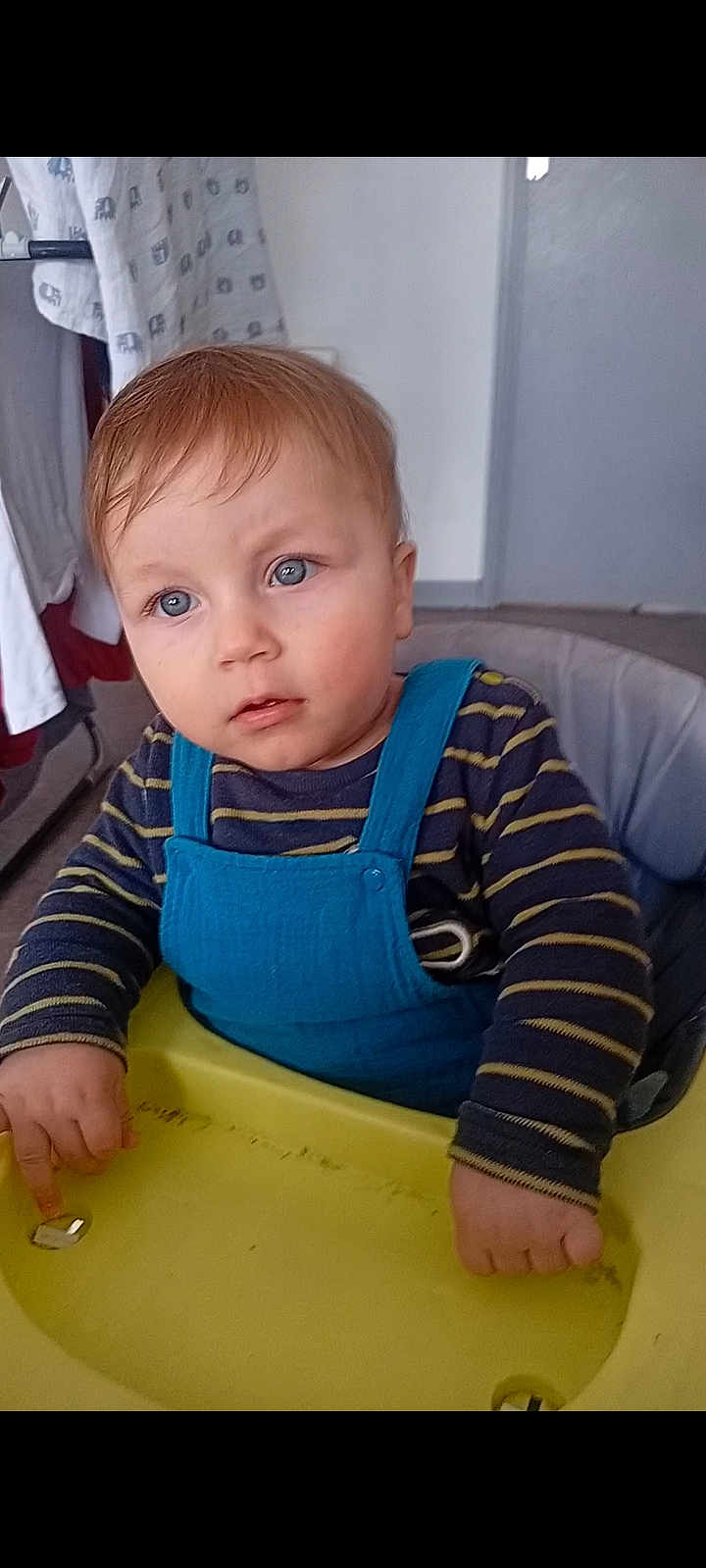 Clément a rejoint le concours — aidez-le/la à gagner de superbes lots ! baby, toddler, child, highchair, tray, blue_overalls, striped_shirt, hands, face, eyes, hair, indoor, sitting, toy, metal_object, cloth_with_elephants, door, wall, floor, portrait