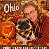 autumn, carved_pumpkin, dog, face, fall, glasses, leaves, ohio, orange, outdoor, person, portrait, pug, pumpkin, scarf, seasonal_decor, state, sweater, text_overlay, woman