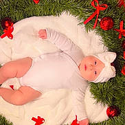 Emely is registered to the contest to win money with this photo: baby, infant, white_onesie, knitted_hat, blanket, wreath, greenery, red_bows, christmas_ornaments, holiday, festive, red_background, cute, chubby_cheeks, lying_down, indoors, soft_texture, decorations, celebration, portrait
