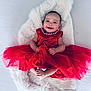 baby, child, red_dress, smile, happy, infant, cute, portrait, fluffy_rug, barefoot, tulle, pearl_necklace, sitting, indoors, person, young_child, celebration, fashion, bright, adorable