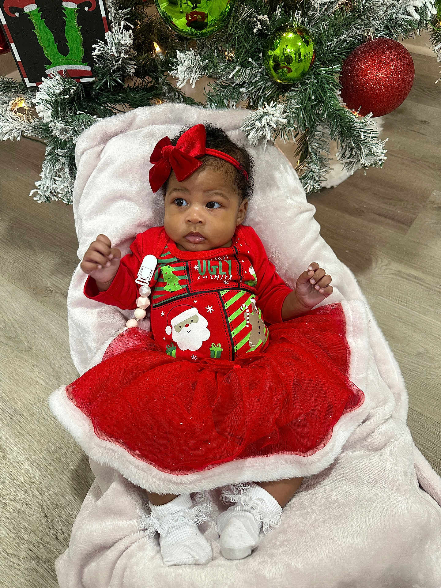 Zora is registered to the contest to win money with this photo: baby, christmas_tree, holiday, red_dress, red_bow, white_blanket, ornaments, green_ornaments, red_ornaments, floor, indoor, festive, cute, child, infant, sock, lace, celebration, seasonal, decor