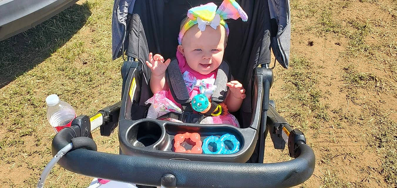 Adalynn is registered to the contest to win money with this photo: auto_part, baby_products, black, chair, child, event, fun, grass, green, happy, headwear, leisure, magenta, person, pink, plant, play, recreation, sitting, smile