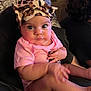baby, infant, child, pink_shirt, leopard_print, headband, bow, hand, leg, face, eyes, person, indoor, seated, curious, expression, blurred_background, clothing, skin, holding