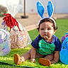 Joseph is registered to the contest to win money with this photo: toddler, child, bunny_ears, easter, outdoor, grass, plush_toy, gift_basket, green_mat, sunny, cute, sitting, blue_shirt, brown_shoes, holiday, spring, face, portrait, playful, decorative