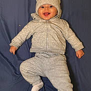 Dylan joined the competition — help win amazing prizes! baby, child, infant, smiling, happy, portrait, lying_down, winter_clothing, knit_hat, jacket, pants, socks, blanket, blue_background, indoor, cozy, cute, face, photography, full_body