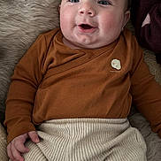 Elio a rejoint le concours — aidez-le/la à gagner de superbes lots ! baby, infant, smiling, drool, brown_clothing, cream_pants, ribbed_texture, fluffy_blanket, happy, cute, portrait, child, person, indoors, cozy, soft_texture, newborn, lying_down, casual_wear, warm_colors