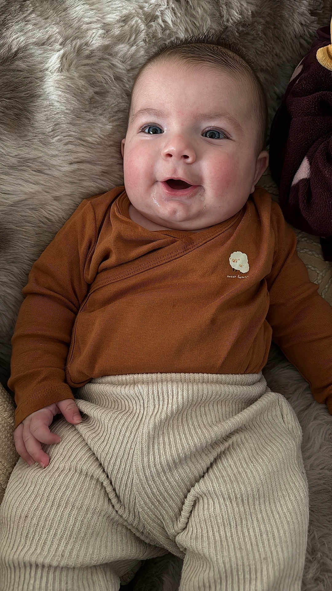 Elio a rejoint le concours — aidez-le/la à gagner de superbes lots ! baby, infant, smiling, drool, brown_clothing, cream_pants, ribbed_texture, fluffy_blanket, happy, cute, portrait, child, person, indoors, cozy, soft_texture, newborn, lying_down, casual_wear, warm_colors