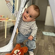 Iris participe au concours pour gagner de l'argent avec cette photo : toddler, child, indoor, floor, wooden_floor, high_chair, stuffed_animal, orange_toy, curious, playful, clothing, striped_shirt, jeans, sock, furniture, home, baby, person, flooring, floor_mat