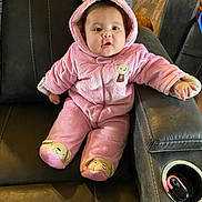 Naomi is registered to the contest to win money with this photo: baby, infant, pink_onesie, hooded_clothing, couch, leather_furniture, cute, indoors, child, baby_clothes, footwear, plush, seated, looking_at_camera, cup_holder, wooden_floor, adorable, warm_clothing, face, expression