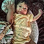 baby, child, infant, yellow_onesie, elephant_design, cushion, patterned_blanket, smiling, happy, lying_down, indoor, face, arms_up, curly_hair, cute, soft_lighting, fabric, comfort, playful, portrait