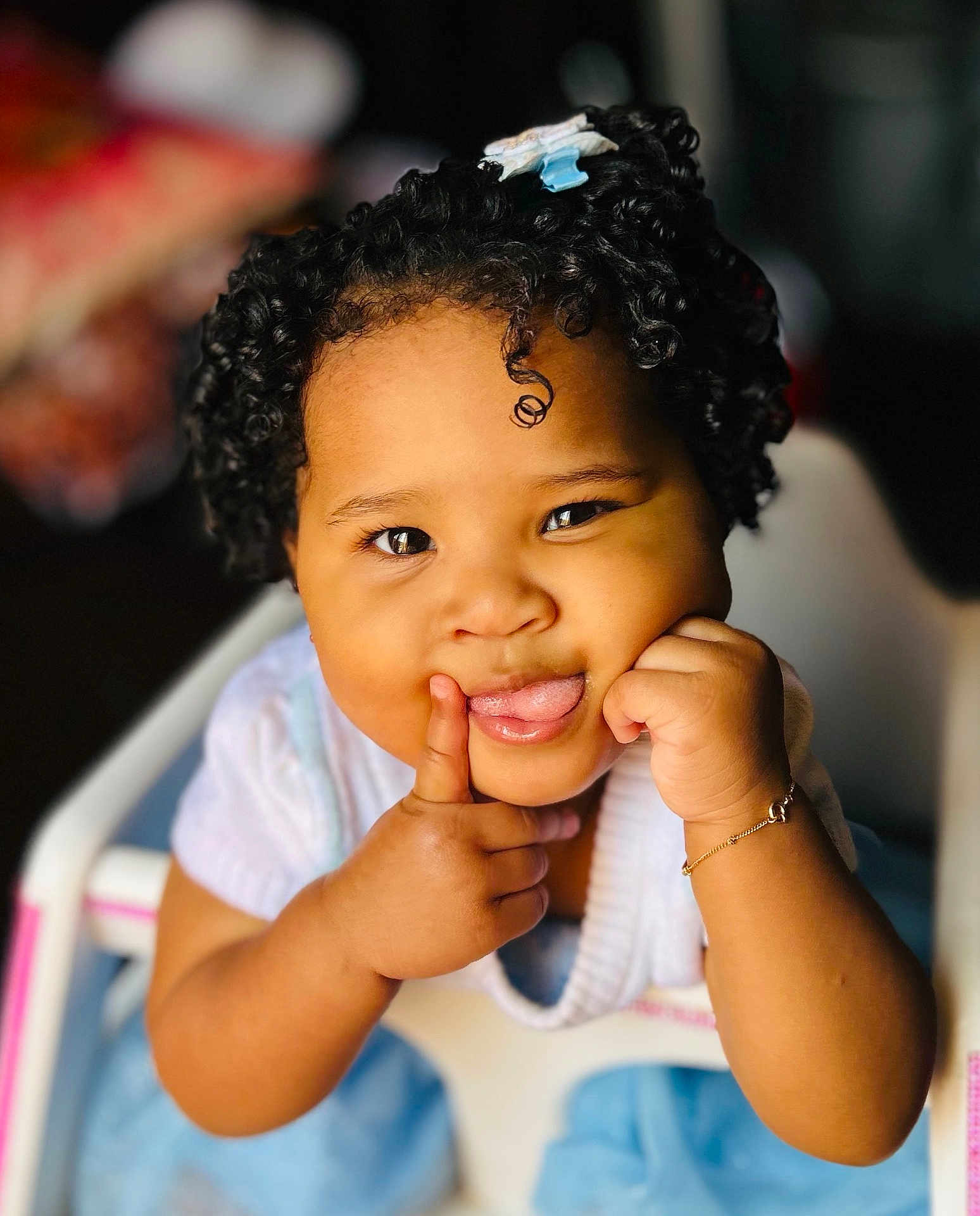 Kaymie is registered to the contest to win money with this photo: toddler, child, curly_hair, tongue_out, high_chair, bracelet, smiling, cute, person, indoors, baby_clothes, face, hand, skin, expression, playful, portrait, sitting, close_up, happy