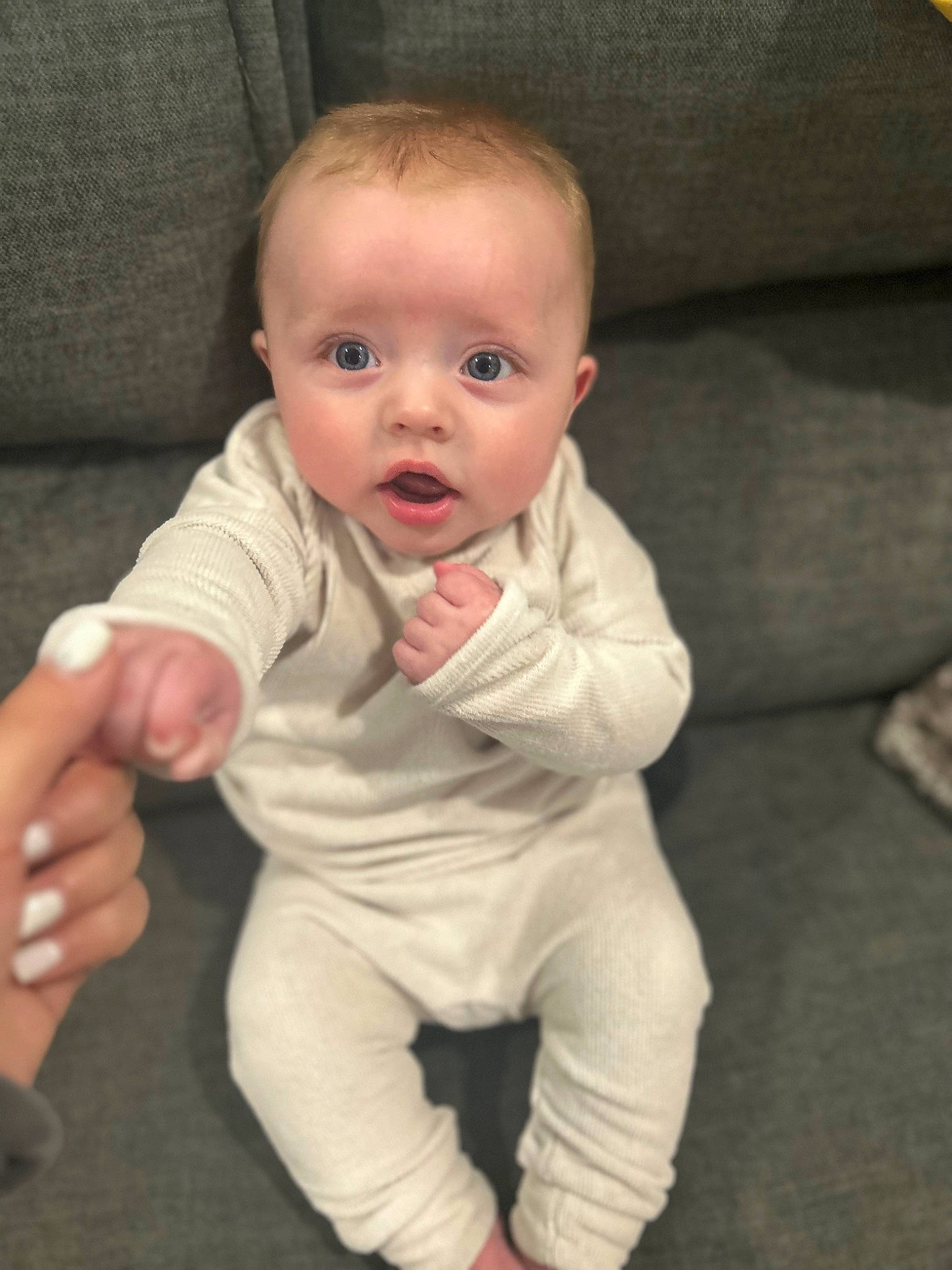 Layton is registered to the contest to win money with this photo: baby, baby_toddler_clothing, cheek, child, comfort, couch, eye, facial_expression, finger, floor, flooring, gesture, hand, iris, nose, person, skin, sleeve, standing, surprise