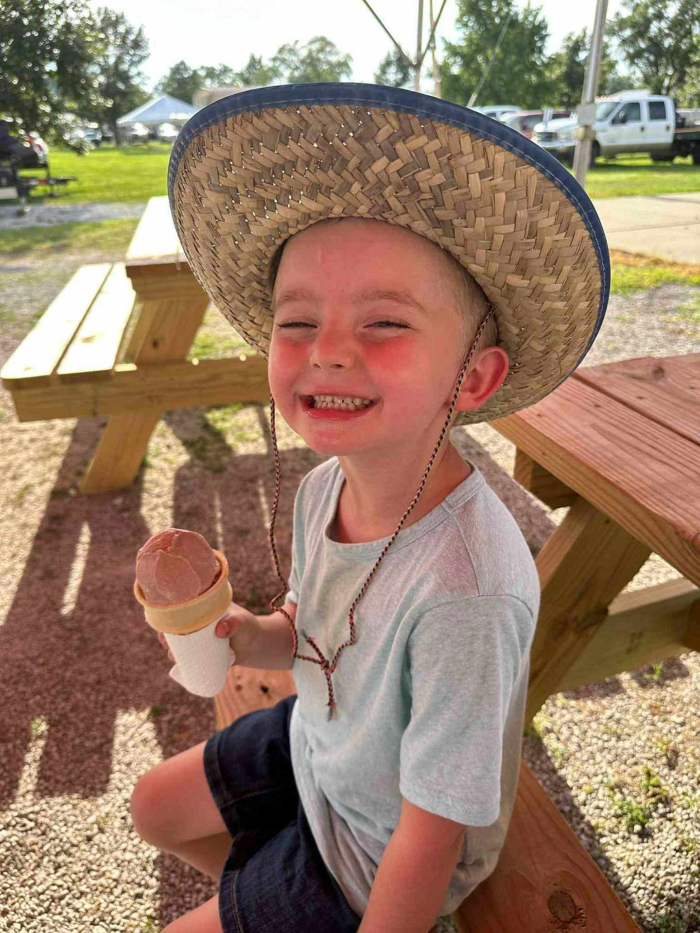 Zayden joined the competition — help win amazing prizes! child, boy, smiling, hat, straw_hat, ice_cream, cone, picnic_bench, outdoor, sunlight, summer, happy, casual_clothing, shorts, tshirt, grass, trees, park, daytime, recreation