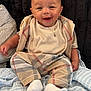 baby, smiling, infant, pajamas, white_socks, blanket, plaid, child, cute, portrait, happy, sitting, face, clothing, indoor, cozy, necklace, soft_toys, comfort, background