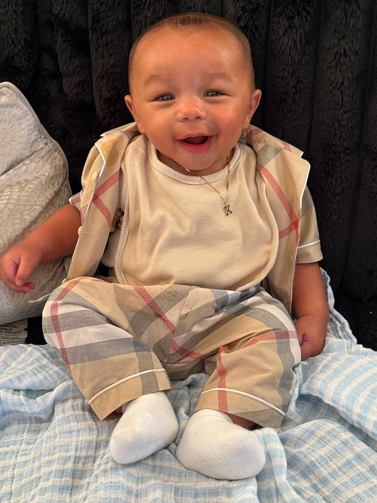Khari is registered to the contest to win money with this photo: baby, smiling, infant, pajamas, white_socks, blanket, plaid, child, cute, portrait, happy, sitting, face, clothing, indoor, cozy, necklace, soft_toys, comfort, background