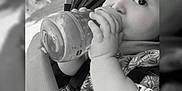Tiziano participe au concours pour gagner de l'argent avec cette photo : baby, baby_accessory, black_and_white, bottle, child, closeup, clothing, cute, expression, face, feeding, hand, infant, outdoor, person, portrait, seatbelt, sitting, stroller, young_child