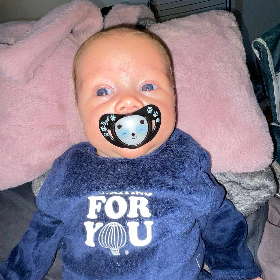 Charle Bource participe au concours pour gagner de l'argent avec cette photo : baby, pacifier, blue_eyes, infant, pink_pillow, blanket, navy_outfit, face, smiling, cute, child, indoors, cozy, soft_texture, lying_down, hand, head, young_child, comfort, sleepwear