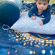 Thiago joined the competition — help win amazing prizes! baby, child, pillow, balloon, outdoor, grass, blanket, curious, face, portrait, young_child, infant, clothing, pattern, star_pattern, blue, black, orange, white, photography