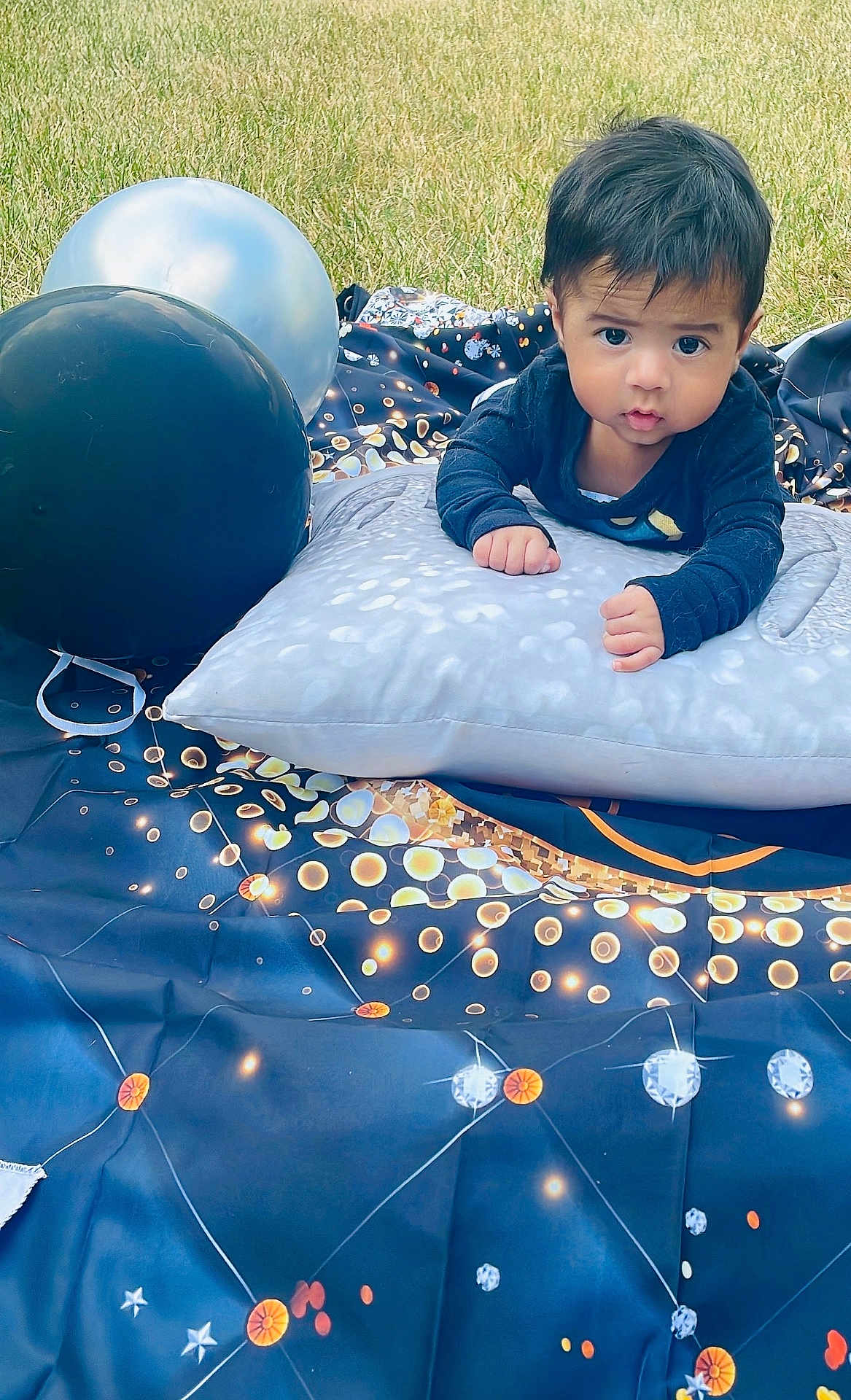 Thiago joined the competition — help win amazing prizes! baby, child, pillow, balloon, outdoor, grass, blanket, curious, face, portrait, young_child, infant, clothing, pattern, star_pattern, blue, black, orange, white, photography
