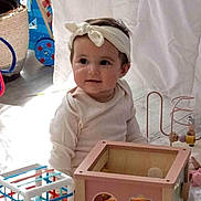 Maëlia participe au concours pour gagner de l'argent avec cette photo : baby, child, headband, toy, wooden_toy, colorful, indoor, curious, sitting, playtime, cute, infant, soft_lighting, white_clothing, floor, homedecor, person, smile, early_childhood, playroom
