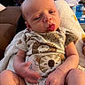 Alban is registered to the contest to win money with this photo: baby, infant, onesie, animal_print, blanket, indoor, person, cute, smiling_face, tongue_out, skin, hand, legs, seated, cozy, child, newborn, soft_lighting, home, casual