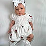 Euphoria is registered to the contest to win money with this photo: baby, child, infant, white_dress, headband, bow, socks, cute, portrait, lying_down, embroidery, red_flowers, soft_lighting, indoor, one_person, young_child, adorable, fashion, closeup, neutral_expression