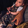 Luka joined the competition — help win amazing prizes! baby, child, person, adult, hand, clothing, overalls, camo, socks, indoor, portrait, cute, expression, holding, skin, face, looking, sitting, dark, cozy