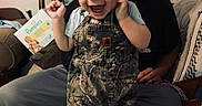 Luka joined the competition — help win amazing prizes! toddler, child, smiling, happy, overalls, camouflage, indoor, living_room, blanket, person, adult, couch, home, furniture, curtains, lamp, diapers, clothing, joy, portrait