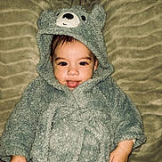 Luka joined the competition — help win amazing prizes! baby, child, face, tongue_out, costume, bear_costume, hood, soft_texture, blanket, cute, playful, smiling, lying_down, indoor, person, infant, cozy, warm_clothing, head, expression